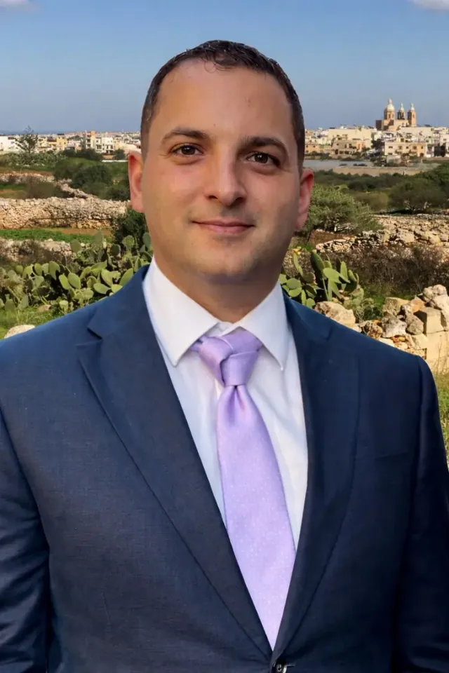 Ryan Tanti wearing a blue suit, with Ħad-Dingli in the background